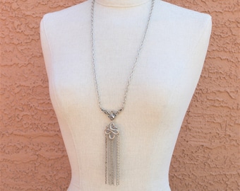 May include: A silver chain necklace with a silver pendant featuring a flower design and a tassel of silver chains.