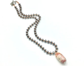 May include: A silver beaded necklace with a long, oval-shaped pendant made of pink and white patterned ceramic.