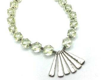 May include: A silver necklace with a fan-shaped pendant and light green faceted beads.