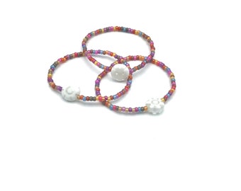May include: Three colorful beaded bracelets with white flower-shaped charms. The bracelets are made of small, colorful beads in shades of pink, purple, orange, and brown.