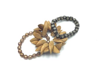 May include: Three bracelets, one with brown wooden beads, one with brown wooden beads shaped like flower petals, and one with black and white beads.