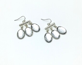 May include: A pair of silver dangle earrings with three clear oval-shaped stones hanging from each earring.