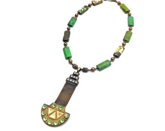 May include: A green and brown beaded necklace with a large, ornate pendant featuring a gold-toned, geometric design and green gemstones.