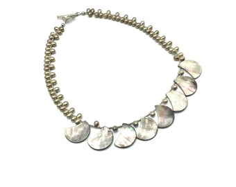 May include: A silver necklace with a row of small, round, beige beads and a row of larger, crescent-shaped, iridescent shell pendants.