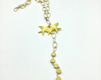 May include: A gold chain necklace with a pair of yellow bird charms and a strand of yellow round beads.