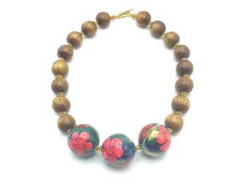 May include: A wooden bead necklace with three larger beads featuring a floral design in shades of red, pink, and green on a dark blue background.