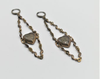 May include: A pair of gold-tone earrings with heart-shaped pendants. The pendants are made of a dark metal with a speckled finish.