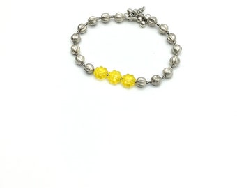 May include: A silver beaded bracelet with a yellow flower charm.