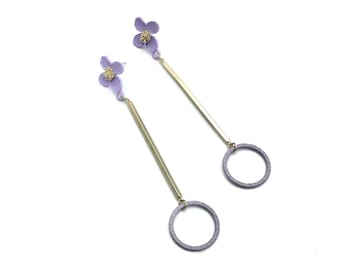 May include: A pair of long, gold dangle earrings with a purple flower charm at the top and a textured purple circle at the bottom.