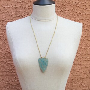 May include: A gold chain necklace with a light blue and white patterned pendant shaped like a teardrop.
