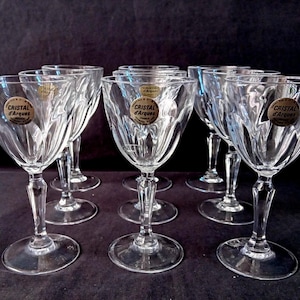 Op de afbeelding: Set van acht heldere kristallen wijnglazen. Elk glas heeft een kenmerkend, getextureerd ontwerp op de kelk en een slanke steel. De glazen hebben een ronde voet en een gouden sticker met "Cristal d'Arques France".