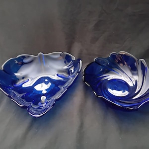 Op de afbeelding: Twee decoratieve glazen schalen. De schalen zijn diepblauw met een zilveren rand. De schalen hebben een unieke, organische vorm, met een golvend, bloembladachtig ontwerp. De schalen zijn waarschijnlijk voor decoratieve doeleinden.