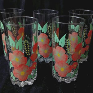 Puede incluir: Un juego de cinco vasos de cristal transparente con un patrón repetitivo de flores rojas con centros amarillos, hojas de color verde claro y espigas de trigo. Cada vaso cilíndrico tiene una base gruesa festoneada y un borde liso.