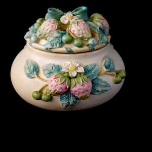 Può includere: Vaso in ceramica color crema con coperchio, ornato con fragole, foglie verdi e un fiocco verde acqua. Il vaso ha una forma rotonda ed è decorato con elementi di frutta e fiori tridimensionali.