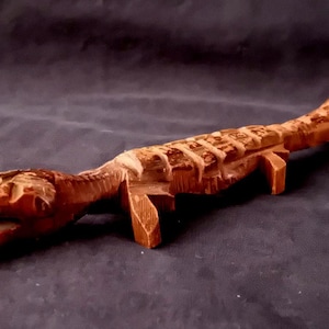 Può includere: Scultura artigianale in legno di alligatore, con un design intagliato dettagliato. L'alligatore è marrone con la bocca aperta ed è posizionato su uno sfondo scuro. La scultura è lunga circa 30 cm.