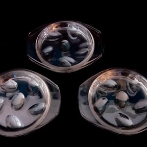 Op de afbeelding: Drie heldere glazen serveerschalen met een ovale vorm en een reeks ovale inkepingen in het midden. De schalen hebben een rechthoekige rand en staan tegen een zwarte achtergrond.