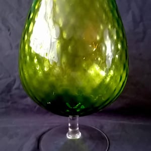 Op de afbeelding: Een groene cognacglas met een getextureerd oppervlak. De grote kom staat op een heldere steel en voet. Het glas heeft een reflecterende kwaliteit, met gele en groene highlights.