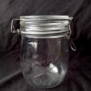 Op de afbeelding: Een glazen voorraadpot van helder glas met een metalen beugelsluiting. De pot heeft een ronde vorm en een wijde opening. Op de voorzijde van het glas is in cursief schrift het woord "Perfect" in reliëf aangebracht.
