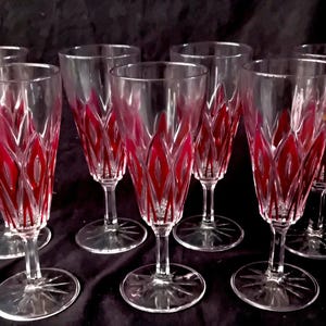 Op de afbeelding: Set van zeven heldere champagneglazen met een rood, bladachtig ontwerp. De glazen hebben een lange steel en een stervormige voet. Het rode ontwerp is zichtbaar door het heldere glas en creëert een decoratief effect.