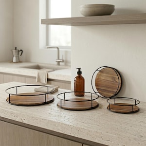 Könnte beinhalten: Eine Sammlung von Serviertabletts aus Holz mit schwarzen Metallrahmen. Die Tabletts sind in verschiedenen Größen erhältlich und stehen auf einer hellen Arbeitsplatte. Eine braune Glasflasche mit Pumpspender ist ebenfalls zu sehen.