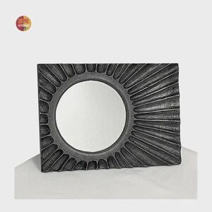 May include: Rectangular, gray-toned mirror with a circular center. The frame has a textured, sunburst design. The mirror is a vintage item, as indicated by the logo in the upper left corner. A decorative piece for home decor.