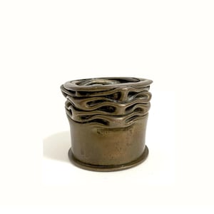 Op de afbeelding: Een cilindervormige metalen houder in bronskleur met een gladde basis en een bovengedeelte dat wordt gekenmerkt door meerdere horizontale, golvende en gevouwen lagen die een gecomprimeerd, geribbeld uiterlijk creëren rondom de omtrek.
