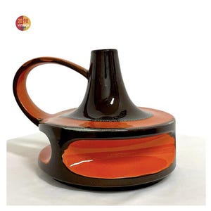Peut inclure: Un bougeoir vintage en céramique, avec un dessus et une poignée marron foncé, passant à une base orange rougeâtre. La pièce a un design circulaire avec une poignée incurvée et une finition brillante. Le texte "20 90 vintage" est dans le coin supérieur gauche.