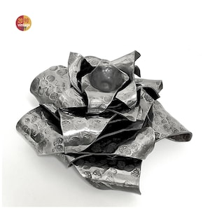 Può includere: Scultura di rosa metallica artigianale con una texture martellata. I petali sono stratificati e arricciati, creando un effetto tridimensionale. La scultura è di colore grigio argento e poggia su uno sfondo bianco. Il logo vintage "20 90 vintage" è in alto a sinistra.