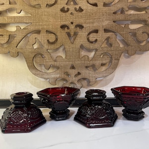 Peut inclure: Un ensemble de quatre pièces en verre rouge profond composé de deux bougeoirs hexagonaux et de deux bols hexagonaux assortis. Chaque pièce présente un motif géométrique texturé en relief sur la surface extérieure, avec une base large.