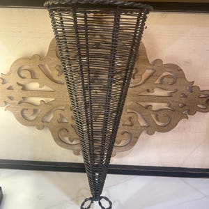 May include: A dark gray wire cone-shaped basket with a woven mesh pattern and a braided rim. The basket is supported by a base constructed from three thin, twisted metal legs that extend outward to form a stable tripod stand for the structure.