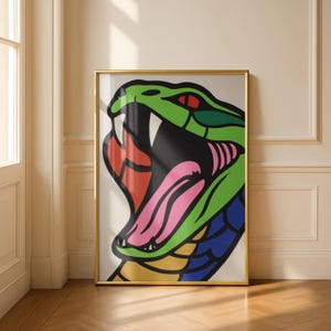 Può includere: Una stampa artistica incorniciata raffigurante un serpente stilizzato e colorato con la bocca aperta. La testa del serpente è verde con occhi rossi, una lingua rosa e una bocca rossa e arancione. L'opera è incorniciata in una cornice dorata e posta su uno sfondo neutro.