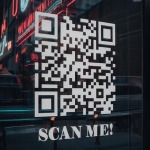 Peut inclure: Un grand code QR blanc est affiché sur une surface vitrée. En dessous du code, les mots "SCAN ME!" sont imprimés en blanc. L'arrière-plan montre une scène de rue floue avec des enseignes au néon.