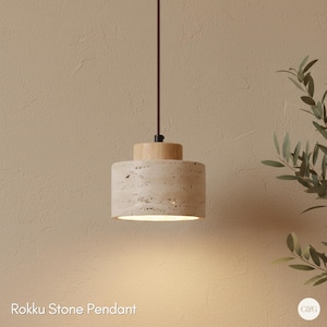 Könnte beinhalten: Eine Pendelleuchte mit einem zylindrischen Steinschirm und einer Holzplatte. Das Licht hängt an einem dunkelbraunen Kabel. Der Text "Rokku Stone Pendant" befindet sich am unteren Bildrand.