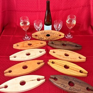 May include: A collection of wooden wine glass holders with the phrases "It's Time For Wine!" and "Corks Are For Quitters" engraved on them. A wine bottle and glasses are also present, all set against a red background.