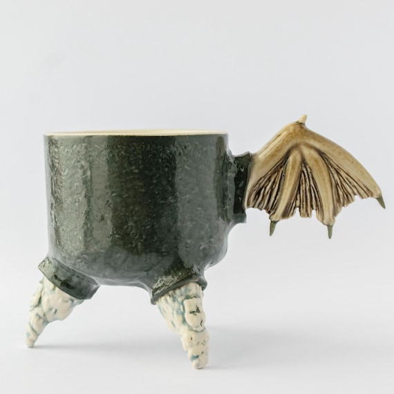 A handmade stoneware mug sprouting actual bat wings — part gothic curiosity cabinet, part functional drinkware, unmistakably one-of-a-kind.