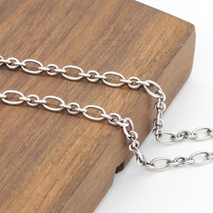 Puede incluir: Una cadena de collar de metal plateado que presenta una serie de eslabones ovalados alargados y uniformes conectados por anillos circulares más pequeños. La cadena tiene un acabado pulido y reflectante, dispuesta en un patrón lineal simple.