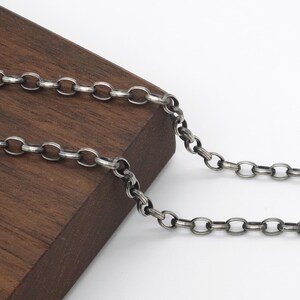 Op de afbeelding: Een donkerzilverkleurige jasseronketting met ronde, uniforme schakels en een licht geoxideerde, matte afwerking. De ketting is aan één uiteinde voorzien van een kleine karabijnsluiting, wat zorgt voor een veilige sluiting van dit sieraad.