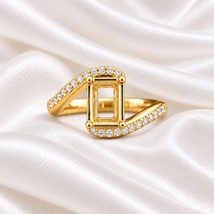 Peut inclure: Une bague en or dotée d'un sertissage rectangulaire central conçu pour accueillir une pierre, flanquée de deux anneaux de style bypass incrustés de petites pierres claires taillées en rond qui s'étendent le long de la tige polie.