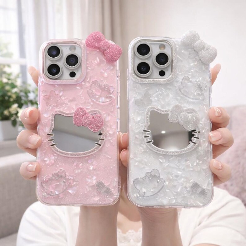 May include: Two phone cases, one pink and one white, featuring a Hello Kitty design. Each case has a bow at the top and a mirrored Hello Kitty face. The pink case has pink glitter, and the white case has white glitter.