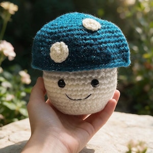 May include: A crocheted mushroom plush toy featuring a dark teal cap with shimmering threads and white circular spots. The stem is off-white with a stitched black smile and two small black plastic eyes embedded in the yarn surface.