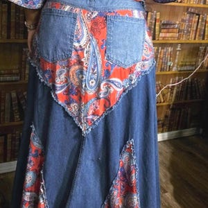 Puede incluir: Una falda larga de mezclilla con un inserto de tela con estampado de cachemira naranja y azul en la parte posterior, a juego con las mangas del top con el mismo estampado. La falda incluye dos bolsillos traseros y bordes deshilachados.