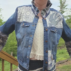 May include: A blue denim jacket featuring a ruffled collar, white lace panels on the shoulders, and a bird appliqué on the left chest. The sleeves are wide and flared, decorated with a blue and white patterned fabric. It has a button-front closure.