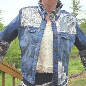 May include: A blue denim jacket featuring a ruffled collar, white lace panels on the upper chest, and a bird appliqué. The sleeves are flared with blue and white patterned fabric, and the front includes button closures and additional patchwork.