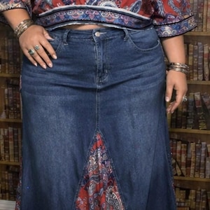 May include: A denim skirt with a flared hem and a red paisley patterned panel. The top is a red and blue paisley print wrap top. The outfit is accessorized with multiple bracelets and necklaces.
