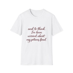 Puede incluir: Camiseta blanca con cuello redondo. La camiseta presenta el texto "and to think I've been worried about my potions final" en una escritura burdeos oscuro. La camiseta está hecha de un material suave.
