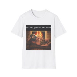 May include: White t-shirt featuring a graphic of a man with a beard and a Sorting Hat in front of a fireplace. The text "So I heard you're into Harry Potter" is above the image. The shirt is a casual wear item.