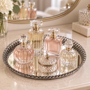 May include: A round mirrored tray with a decorative metal rim holds four glass perfume bottles and a small lidded crystal jar. The collection includes two spherical bottles, one tall rectangular bottle, and one square bottle, all featuring clear glass and gold-toned accents.