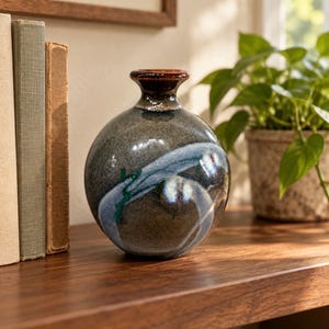 May include: A spherical ceramic vase with a glossy finish, featuring a dark gray and brown mottled base color with a prominent, swirling light blue glaze accent that wraps around the center and a dark brown rim at the narrow neck.