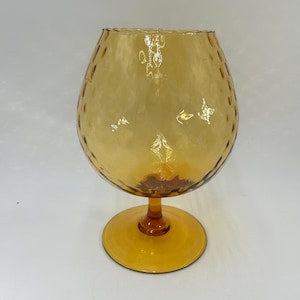 May include: Amber-colored, stemmed glass with a textured, patterned bowl. The glass has a wide, rounded bowl and a circular base. The stem and base are the same color as the bowl. The glass is likely used for serving beverages.