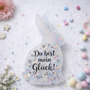 Pode incluir: Uma caneca de cerâmica branca com uma alça preta e o texto "But First, Coffee" em negrito preto. A caneca está sobre um fundo desfocado, destacando seu design simples.